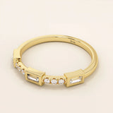 Side angle view of a 14k solid yellow gold band with baguette cut moissanite center stone and round brilliant cut moissanite accents in a modern bezel and prong setting