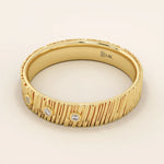 Side angle view of a 14k solid yellow gold wide wedding band with wood grain texture and three bezel set round brilliant cut moissanite stones, artistic and unique fine jewelry