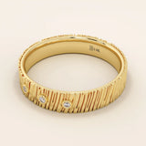 Side angle view of a 14k solid yellow gold wide wedding band with wood grain texture and three bezel set round brilliant cut moissanite stones, artistic and unique fine jewelry