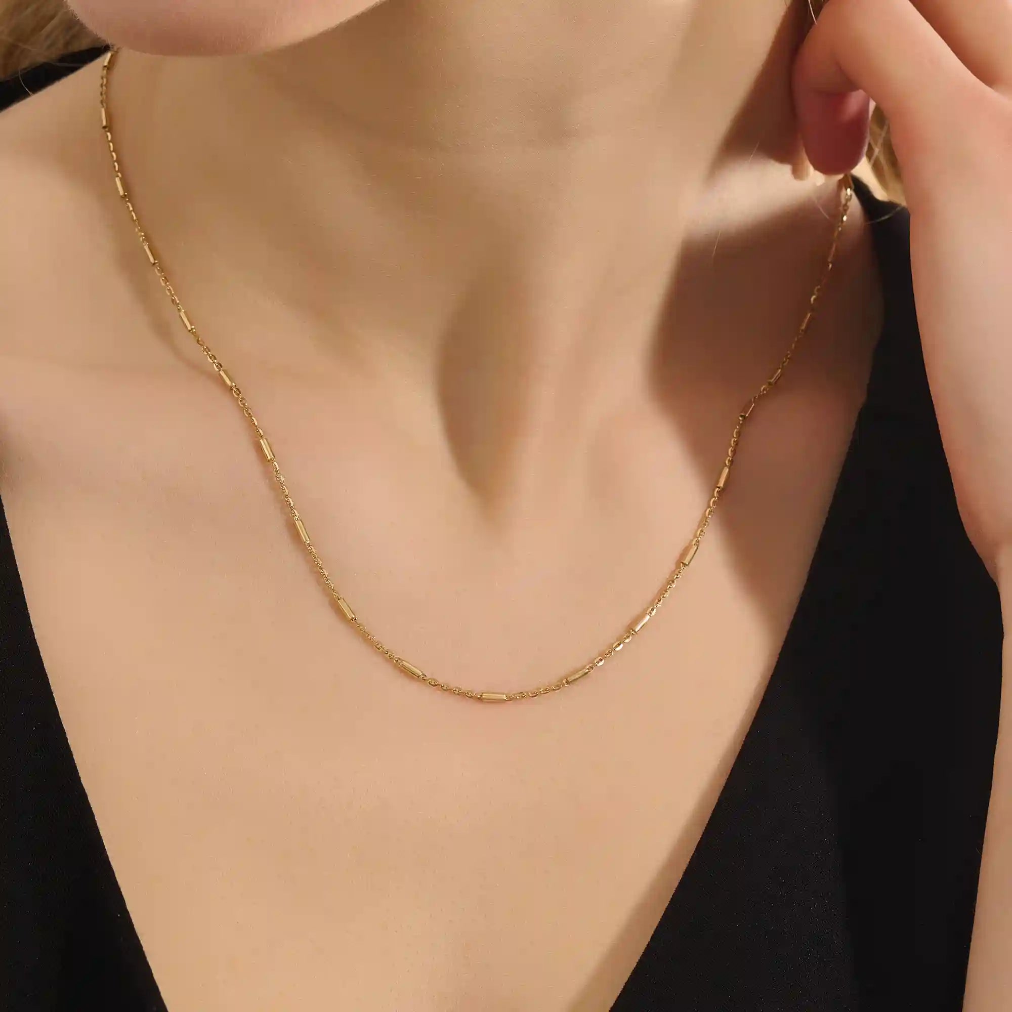 Woman wearing a 14k solid gold bar chain necklace with clean, linear links. A contemporary and elegant gold piece. Perfect for daily wear or stacking.