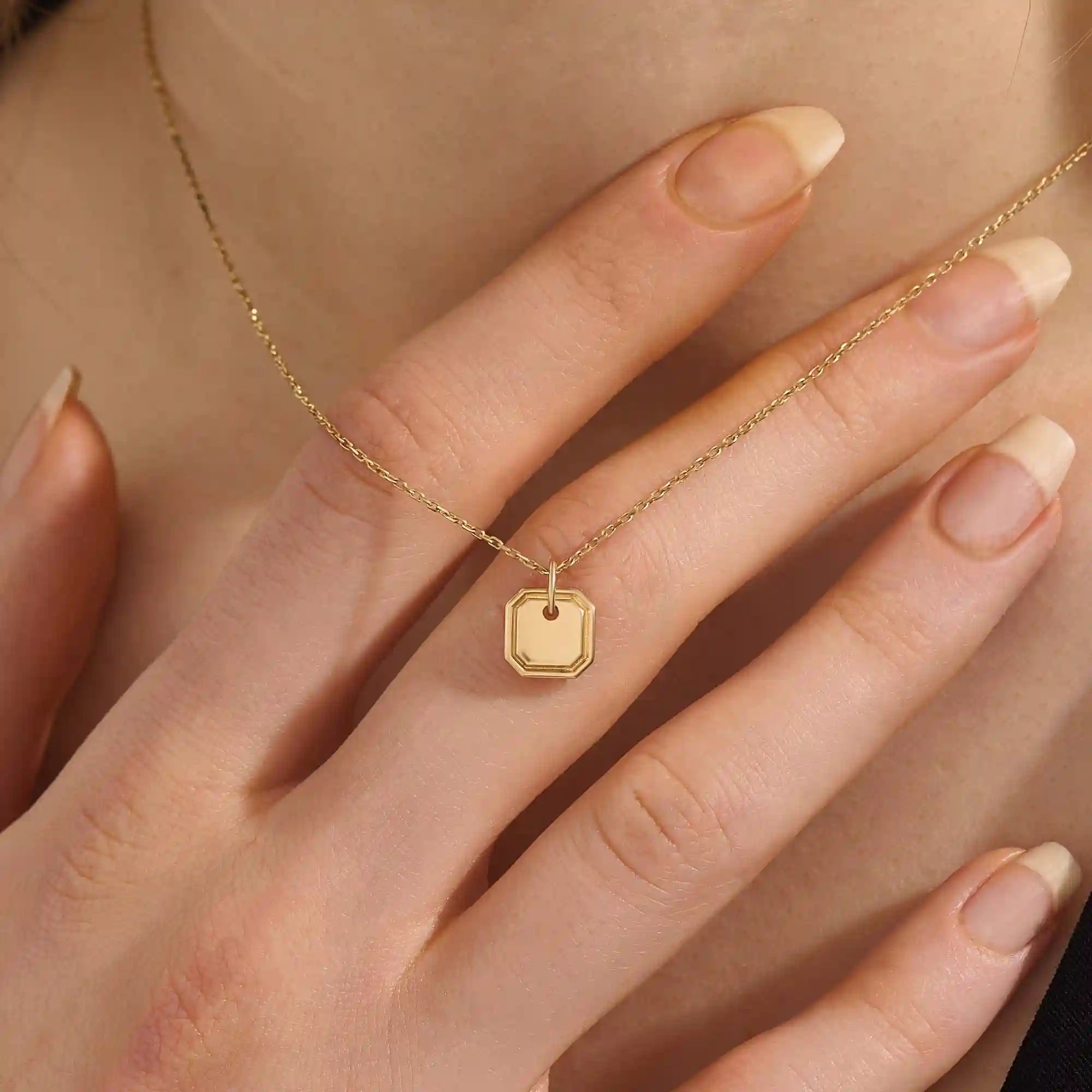 Woman wearing a 14k solid gold dainty octagon pendant necklace. Lightweight and easy-to-style gold charm. Perfect for daily looks or as a layering piece.