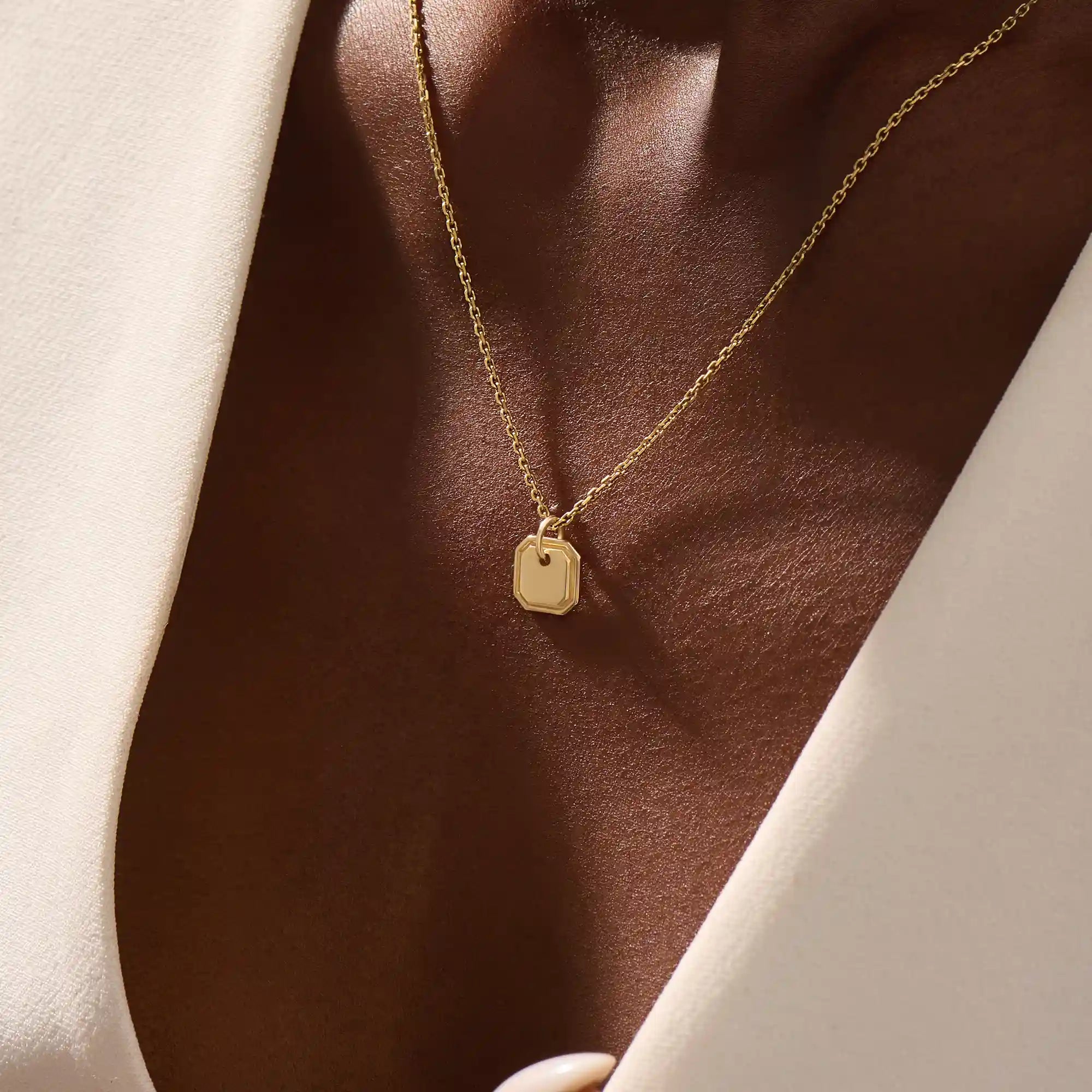 Woman wearing a 14k solid gold dainty octagon pendant necklace. Lightweight and easy-to-style gold charm. Perfect for daily looks or as a layering piece.