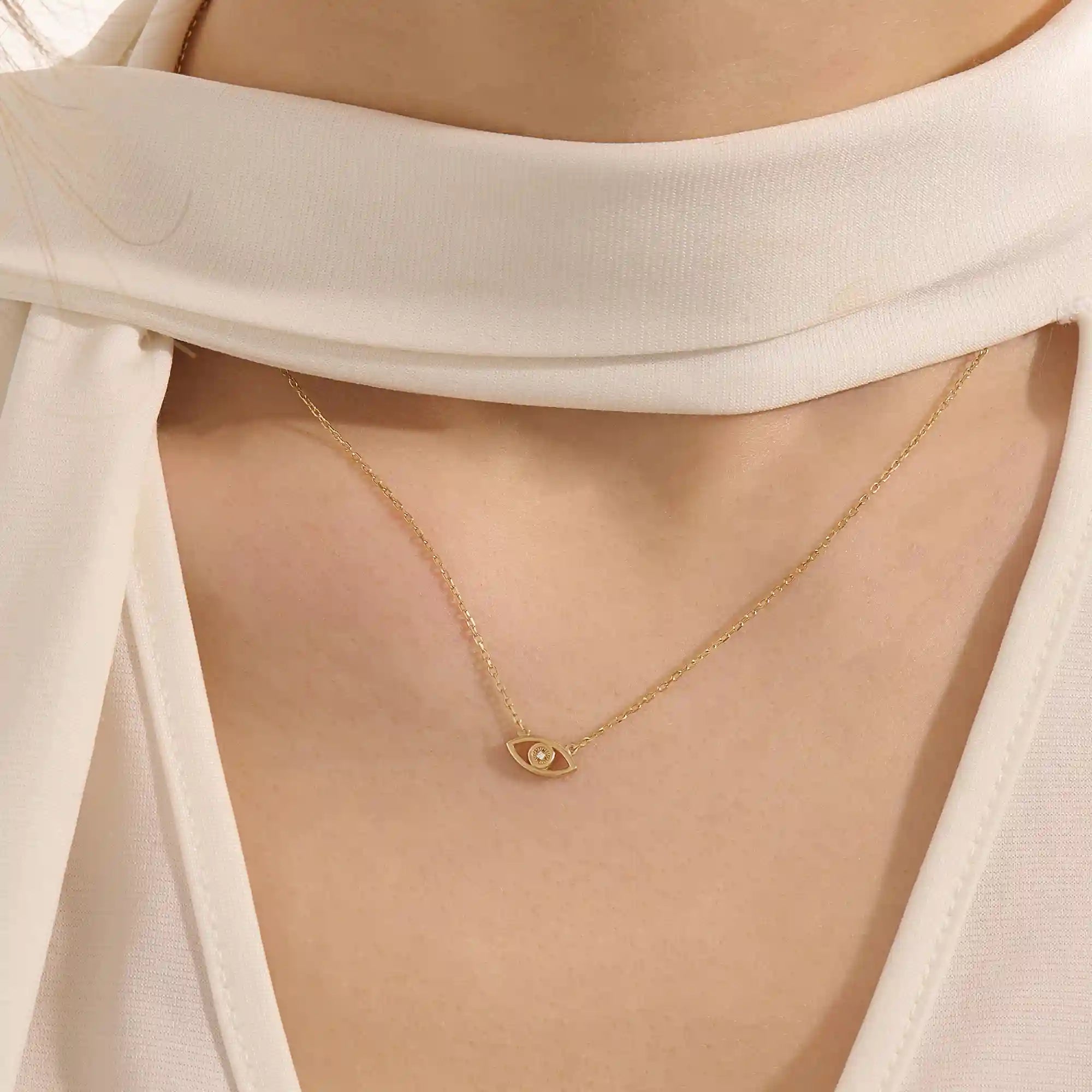 Woman wearing a 14k solid gold evil eye necklace resting at the collarbone. A symbolic and dainty gold design for daily style. Great for layering or wearing solo.