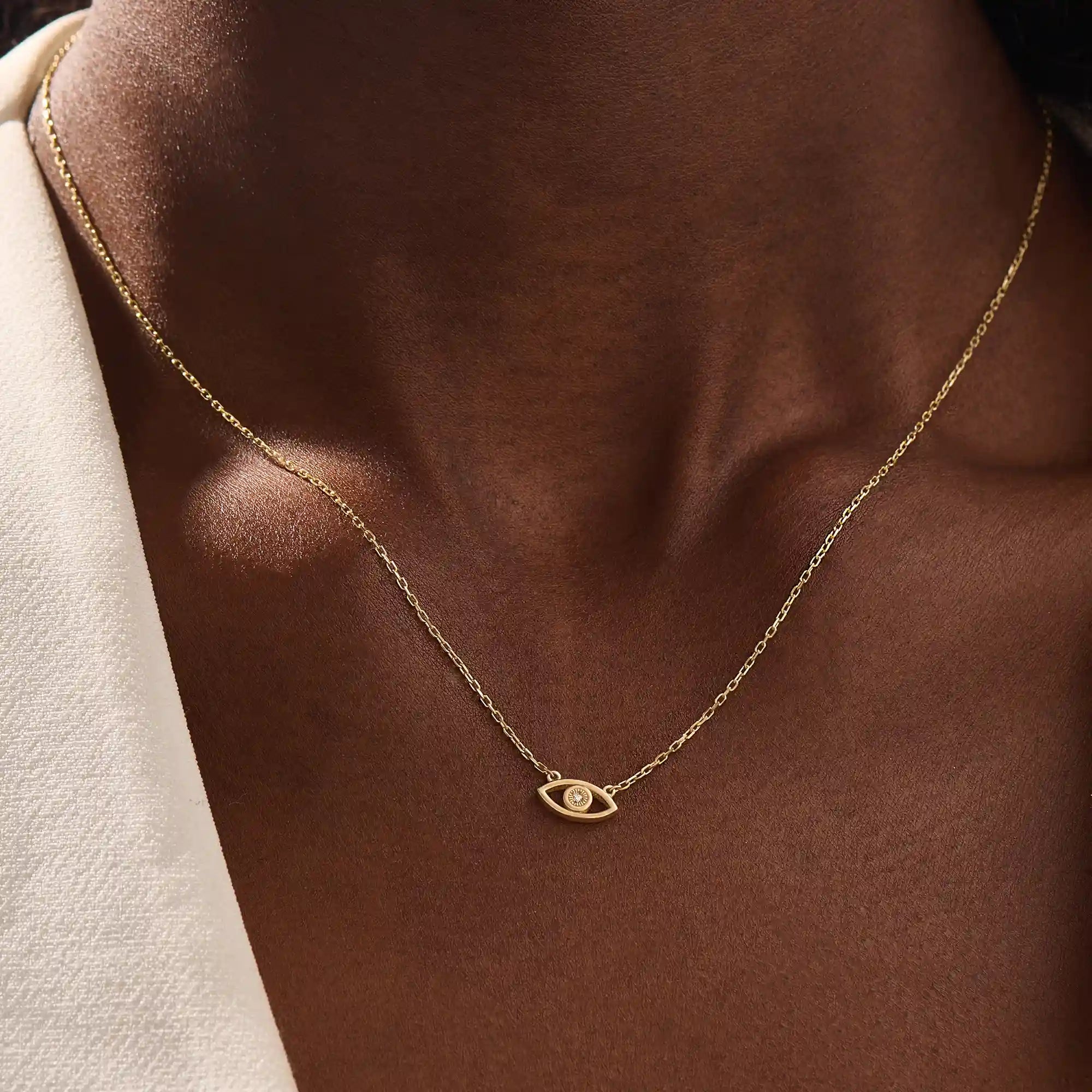 Woman wearing a 14k solid gold evil eye necklace resting at the collarbone. A symbolic and dainty gold design for daily style. Great for layering or wearing solo.