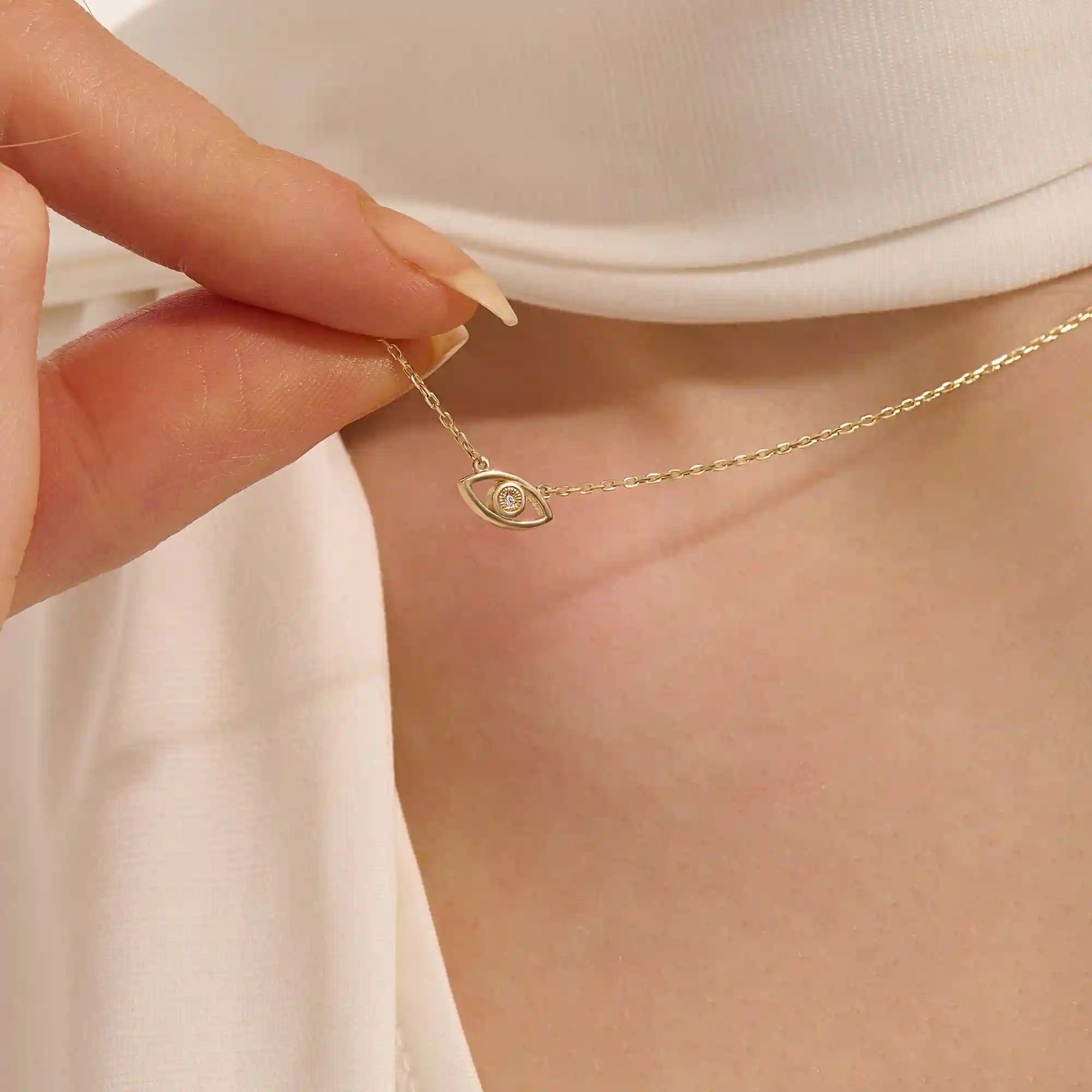 Woman wearing a 14k solid gold evil eye necklace resting at the collarbone. A symbolic and dainty gold design for daily style. Great for layering or wearing solo.