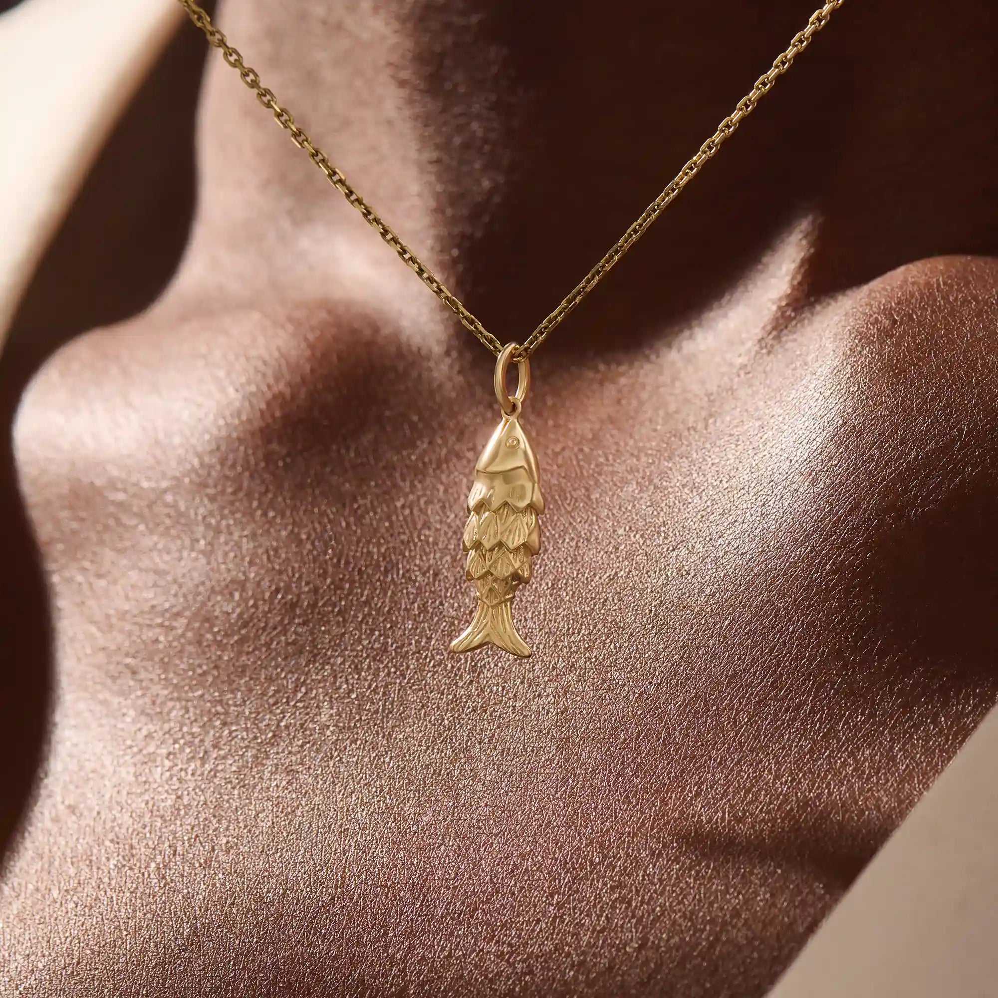 Woman wearing a 14k solid gold fish necklace with a sleek and dainty silhouette. Meaningful and minimalist jewelry piece. Perfect for casual styling or layering.