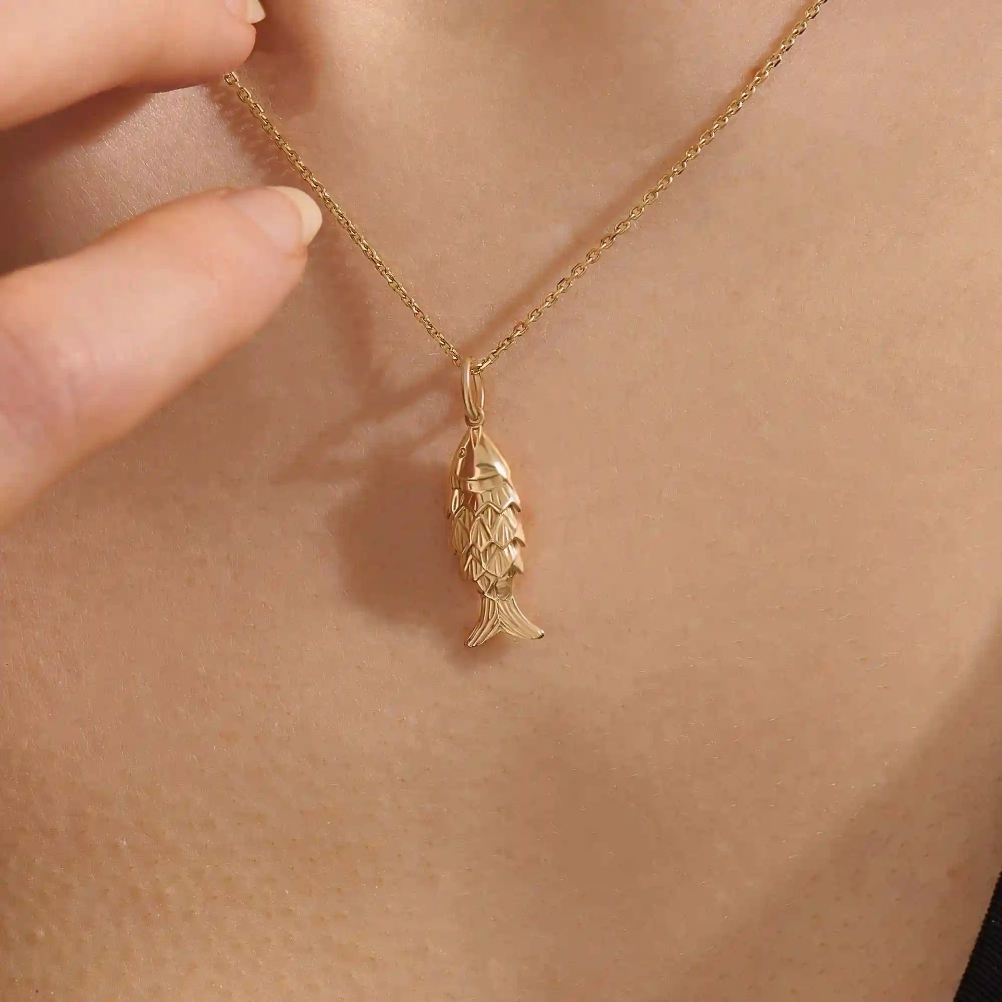 Woman wearing a 14k solid gold fish necklace with a sleek and dainty silhouette. Meaningful and minimalist jewelry piece. Perfect for casual styling or layering.