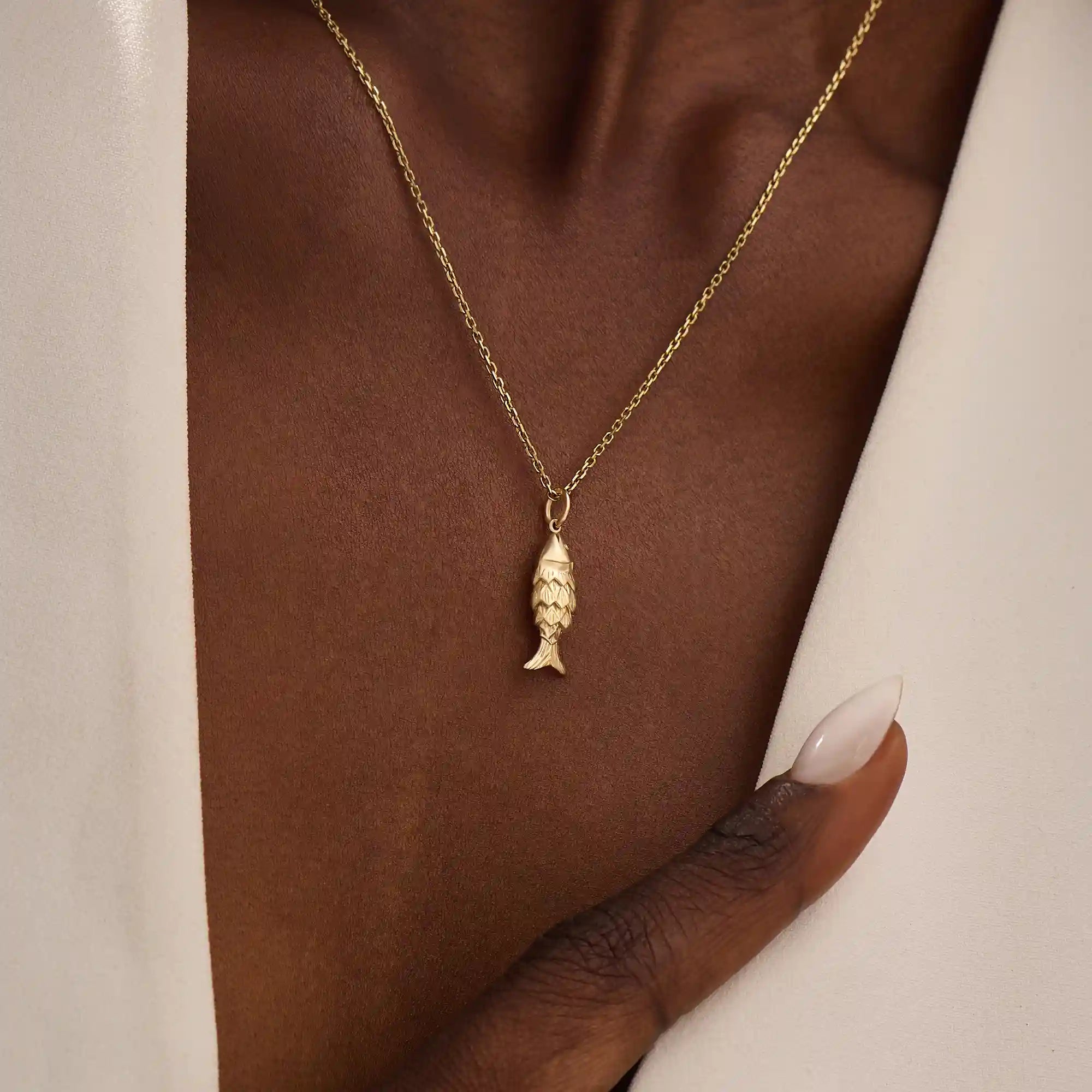 Woman wearing a 14k solid gold fish necklace with a sleek and dainty silhouette. Meaningful and minimalist jewelry piece. Perfect for casual styling or layering.