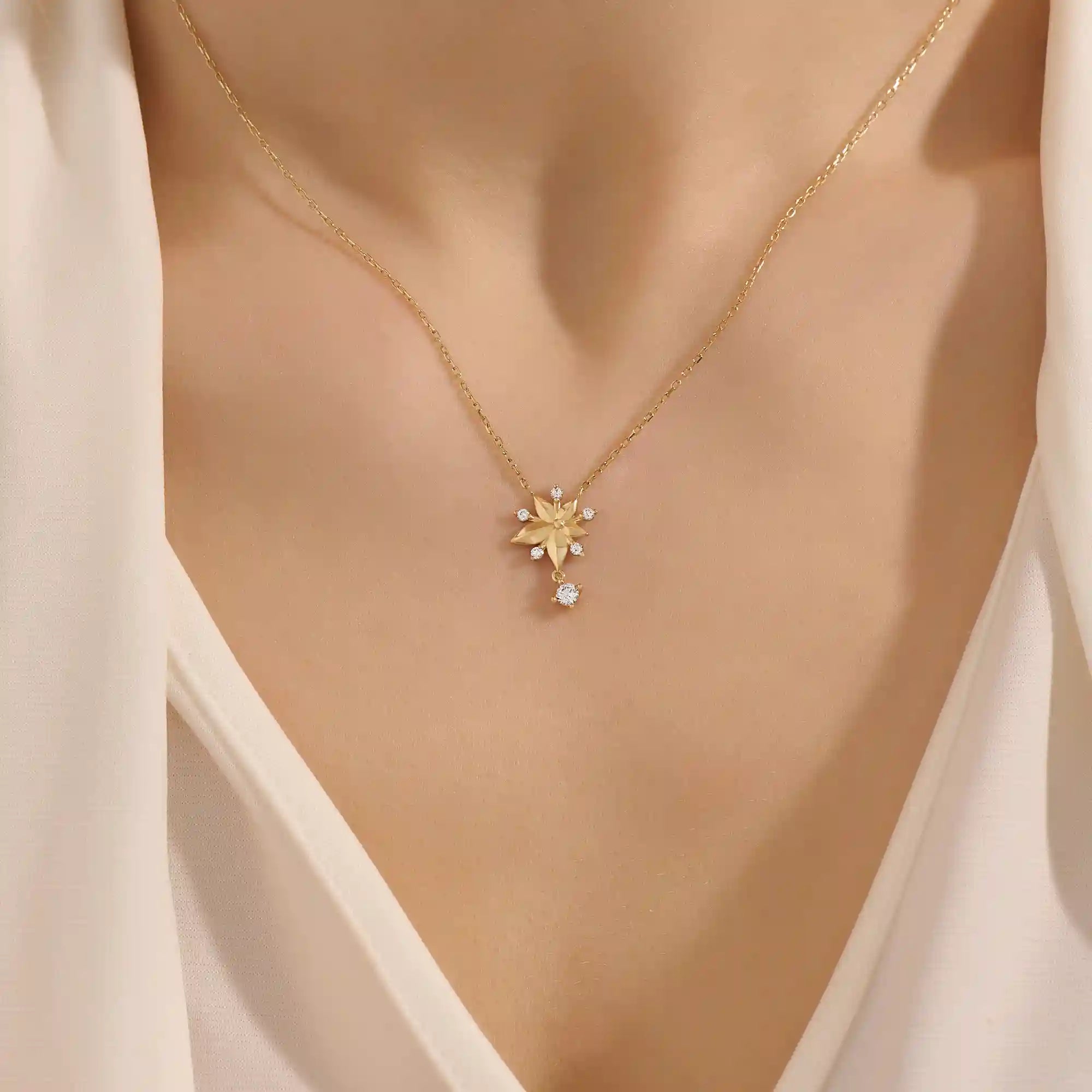 Woman wearing a 14k solid gold flower necklace with five petals and a sparkling dangling moissanite. Nature-inspired and graceful gold jewelry. Perfect for soft, romantic styling.