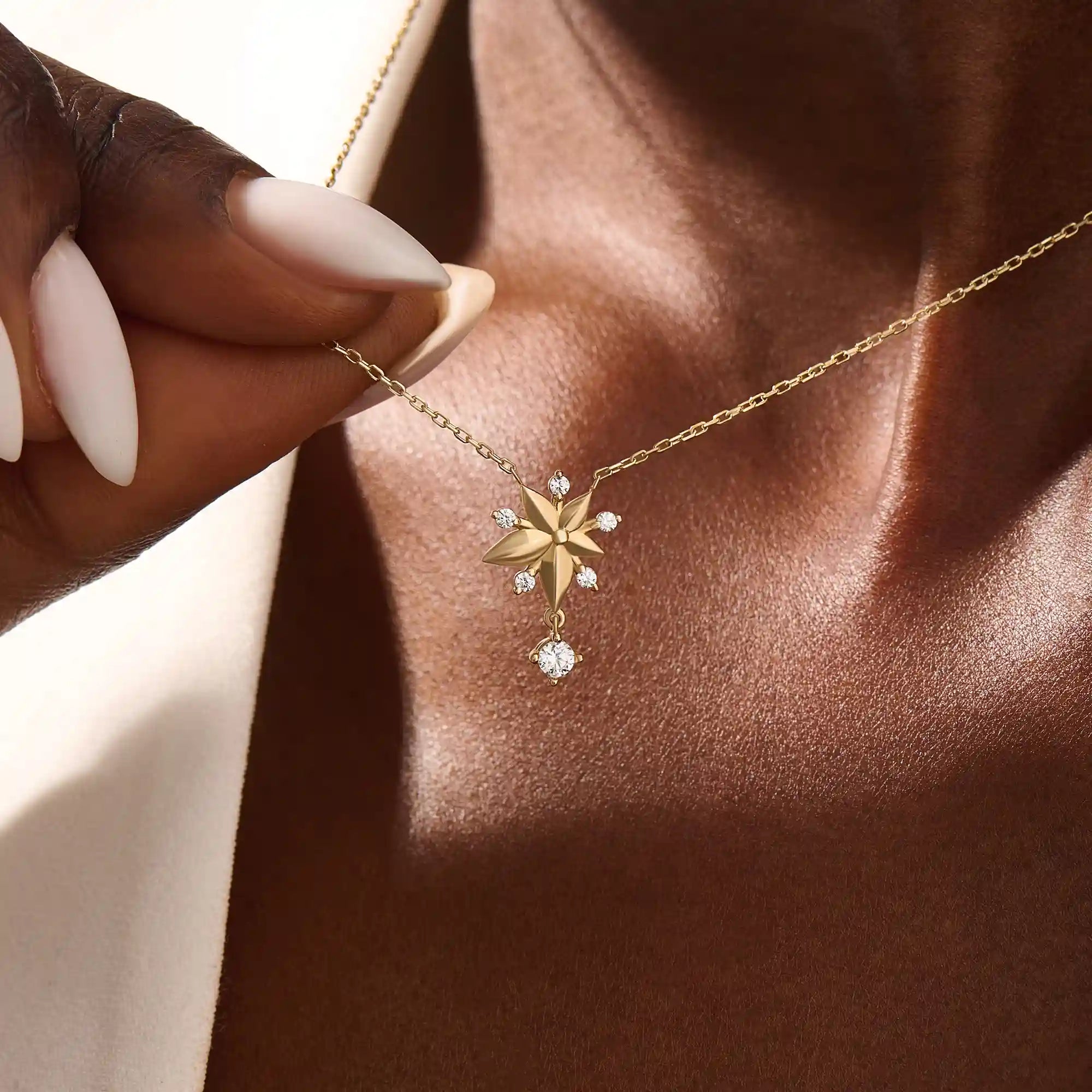 Woman wearing a 14k solid gold flower necklace with five petals and a sparkling dangling moissanite. Nature-inspired and graceful gold jewelry. Perfect for soft, romantic styling.