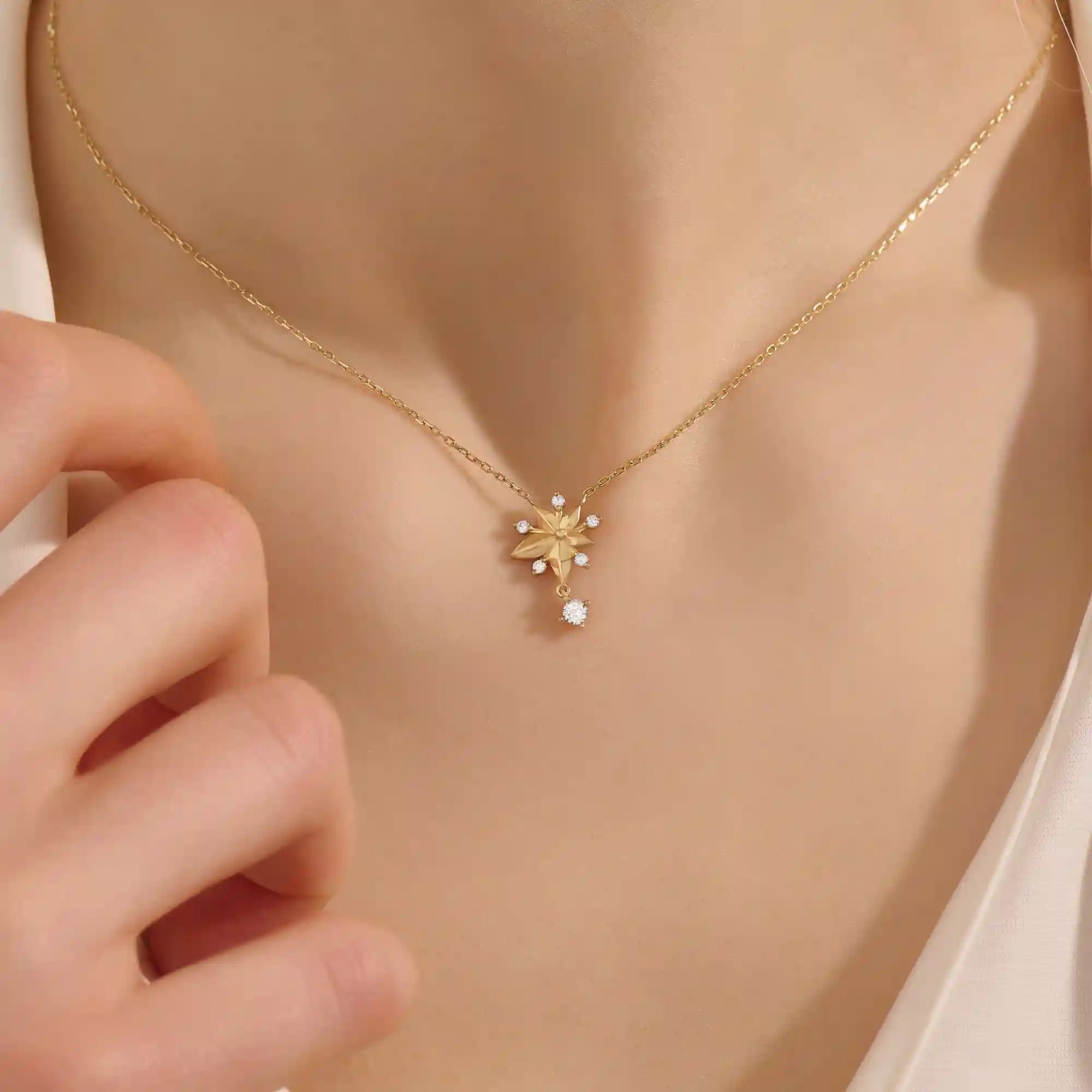 Woman wearing a 14k solid gold flower necklace with five petals and a sparkling dangling moissanite. Nature-inspired and graceful gold jewelry. Perfect for soft, romantic styling.