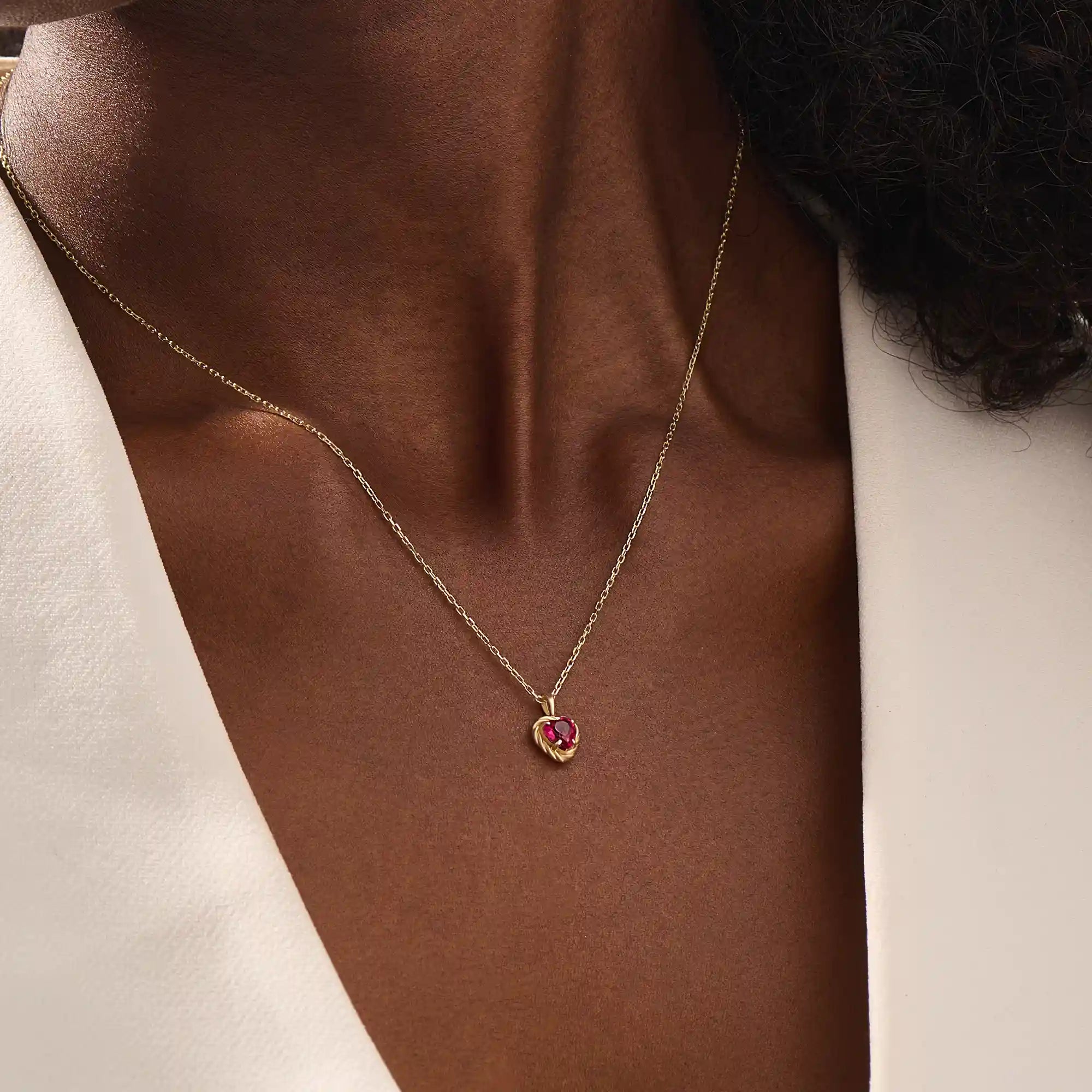 Woman wearing a 14k solid gold heart necklace with a vibrant lab-created ruby. Romantic and timeless gemstone pendant. Perfect for layering or wearing solo.