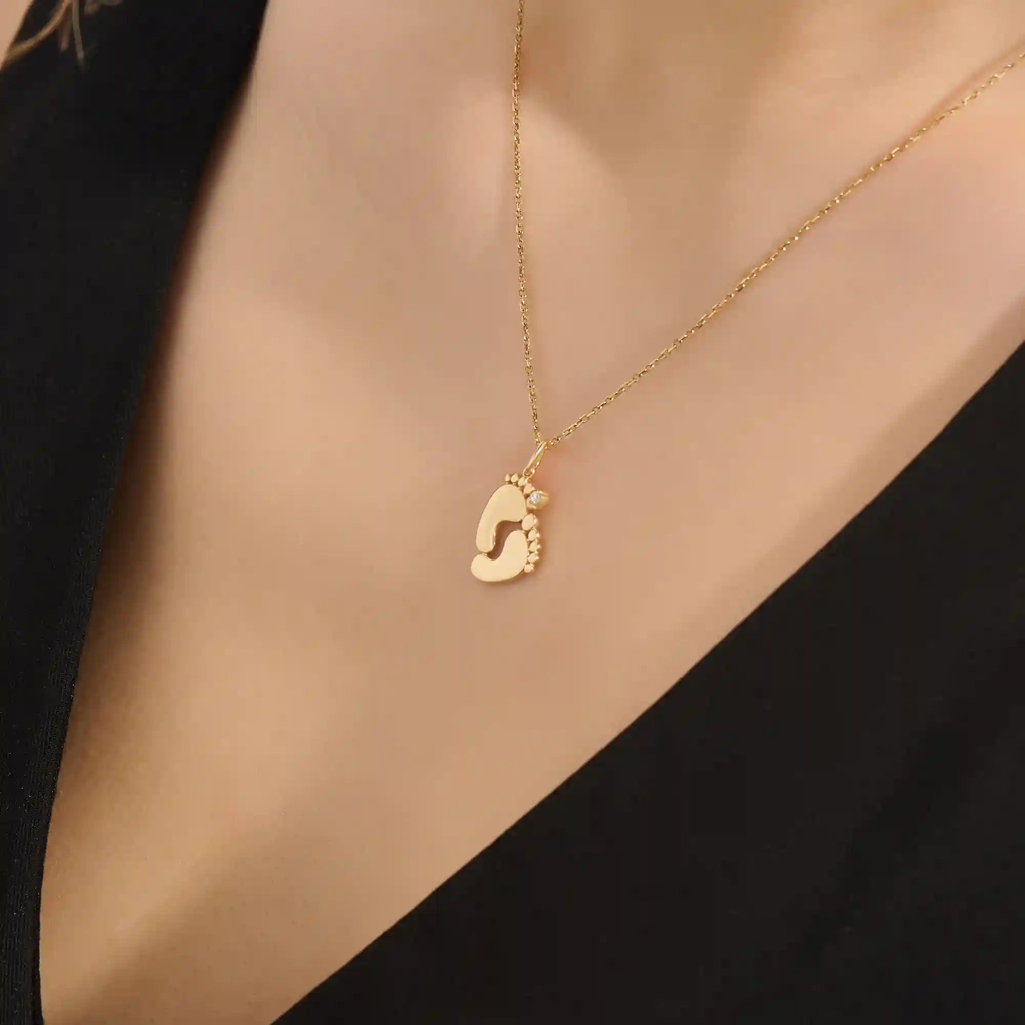 Woman wearing a 14k solid gold necklace with a baby foot pendant and sparkling moissanite detail. A meaningful and dainty gold piece celebrating motherhood and love. Ideal for layering or as a daily keepsake.