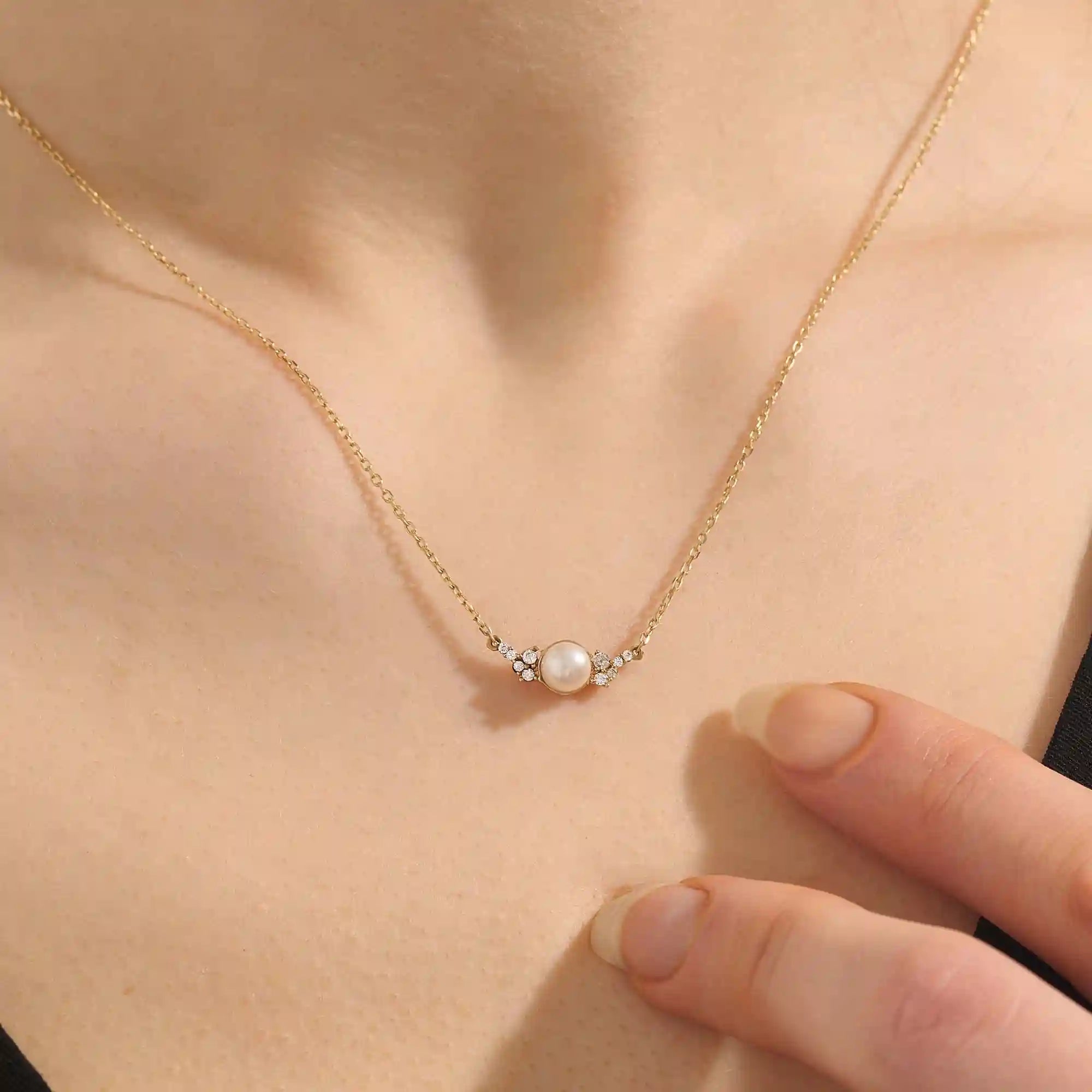 Woman wearing a 14k solid gold pearl necklace with sparkling moissanite clusters flanking the center pearl. Chic and refined gold necklace for women. Great for layering or special occasions.