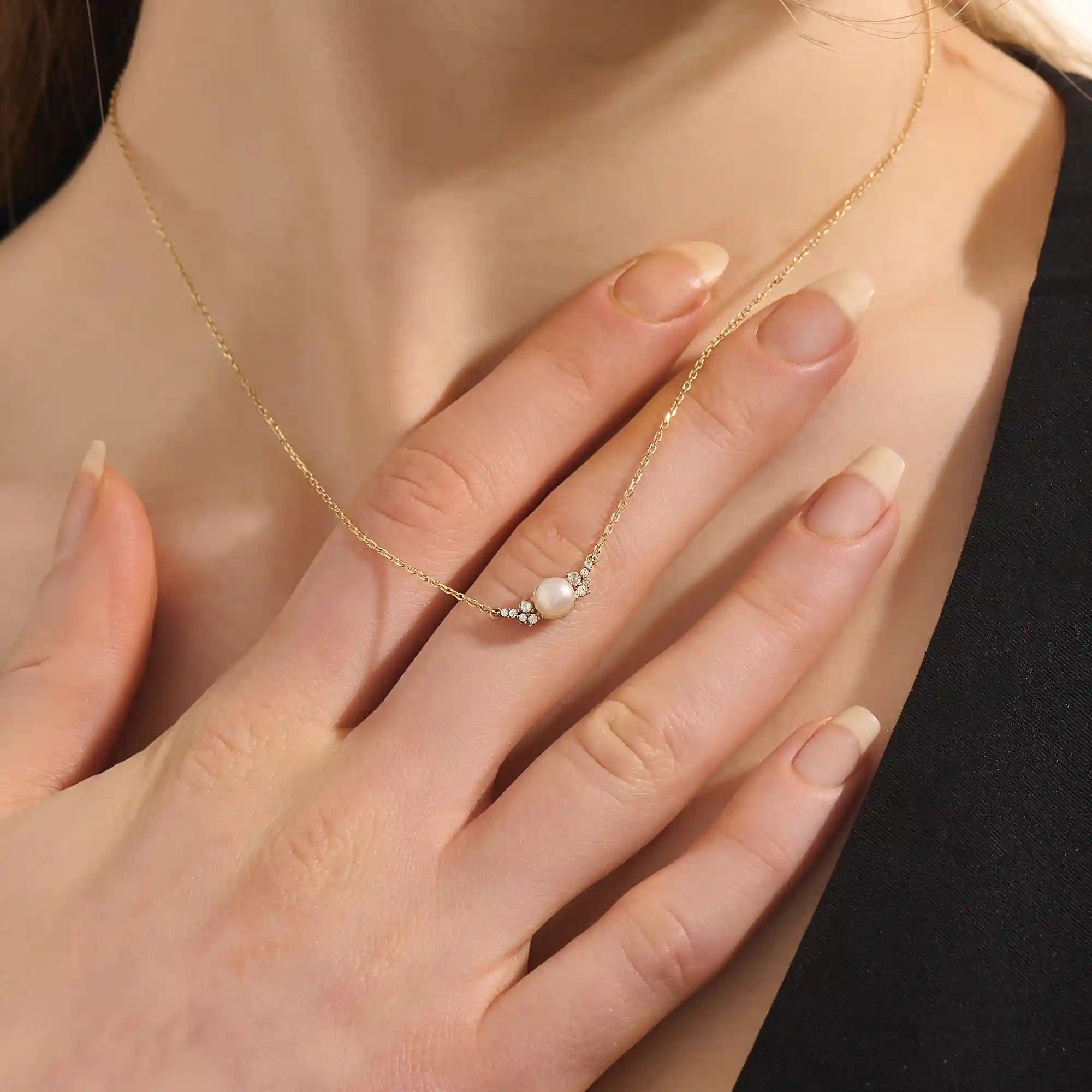 Woman wearing a 14k solid gold pearl necklace with sparkling moissanite clusters flanking the center pearl. Chic and refined gold necklace for women. Great for layering or special occasions.