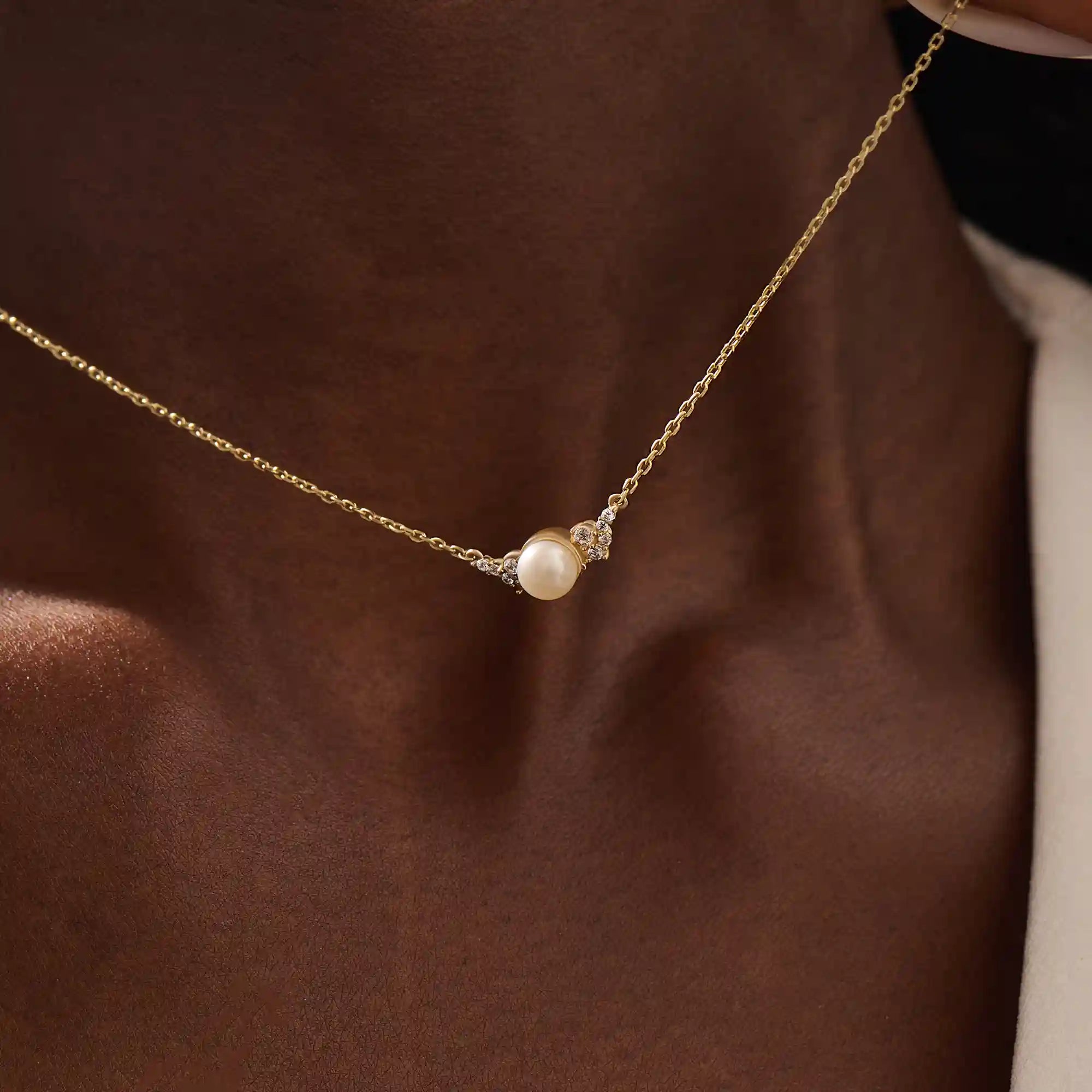 Woman wearing a 14k solid gold pearl necklace with sparkling moissanite clusters flanking the center pearl. Chic and refined gold necklace for women. Great for layering or special occasions.