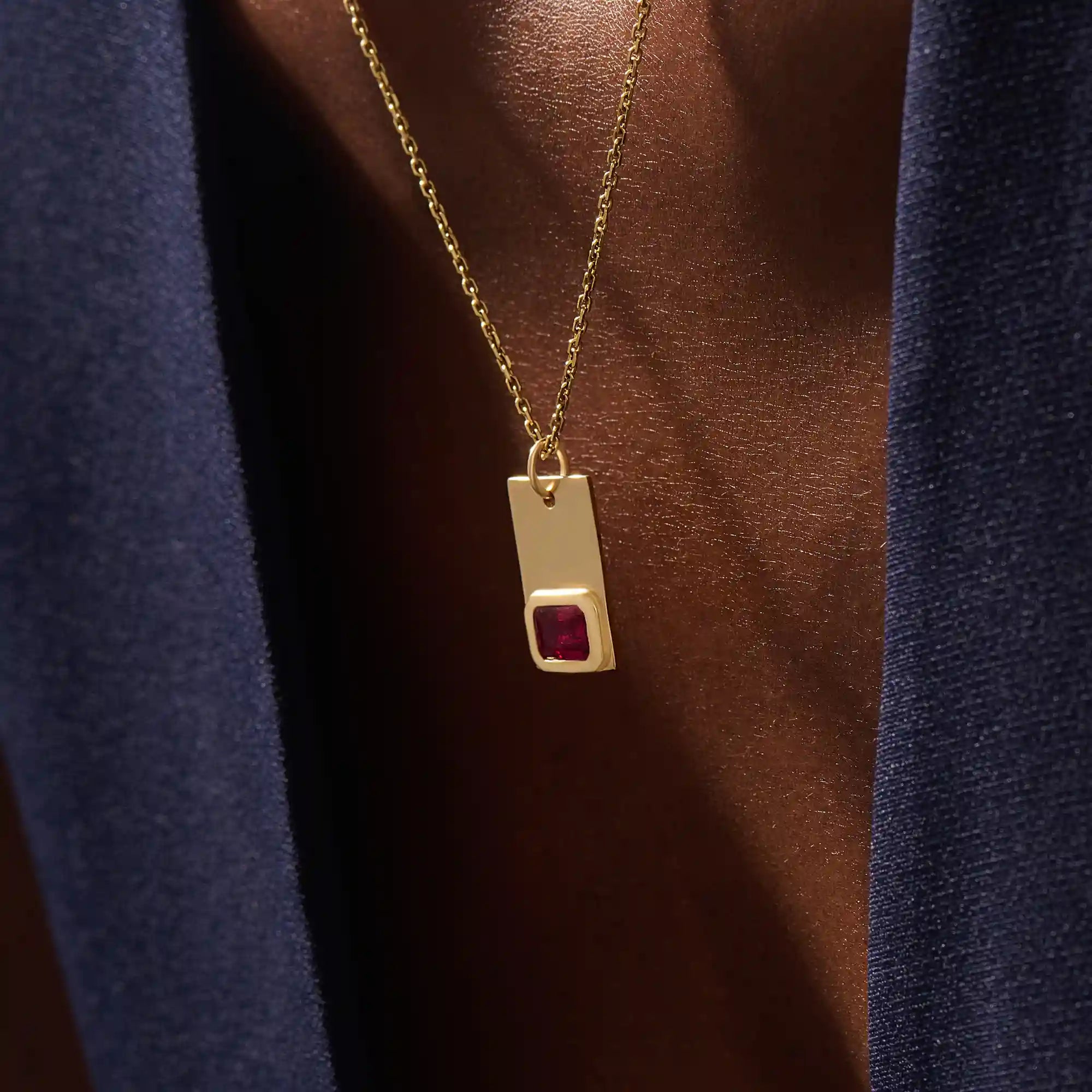 Woman wearing a 14k solid gold rectangle pendant necklace featuring an emerald-cut lab-created ruby in bezel setting. Striking birthstone jewelry with timeless elegance. Ideal for everyday wear or special occasions.