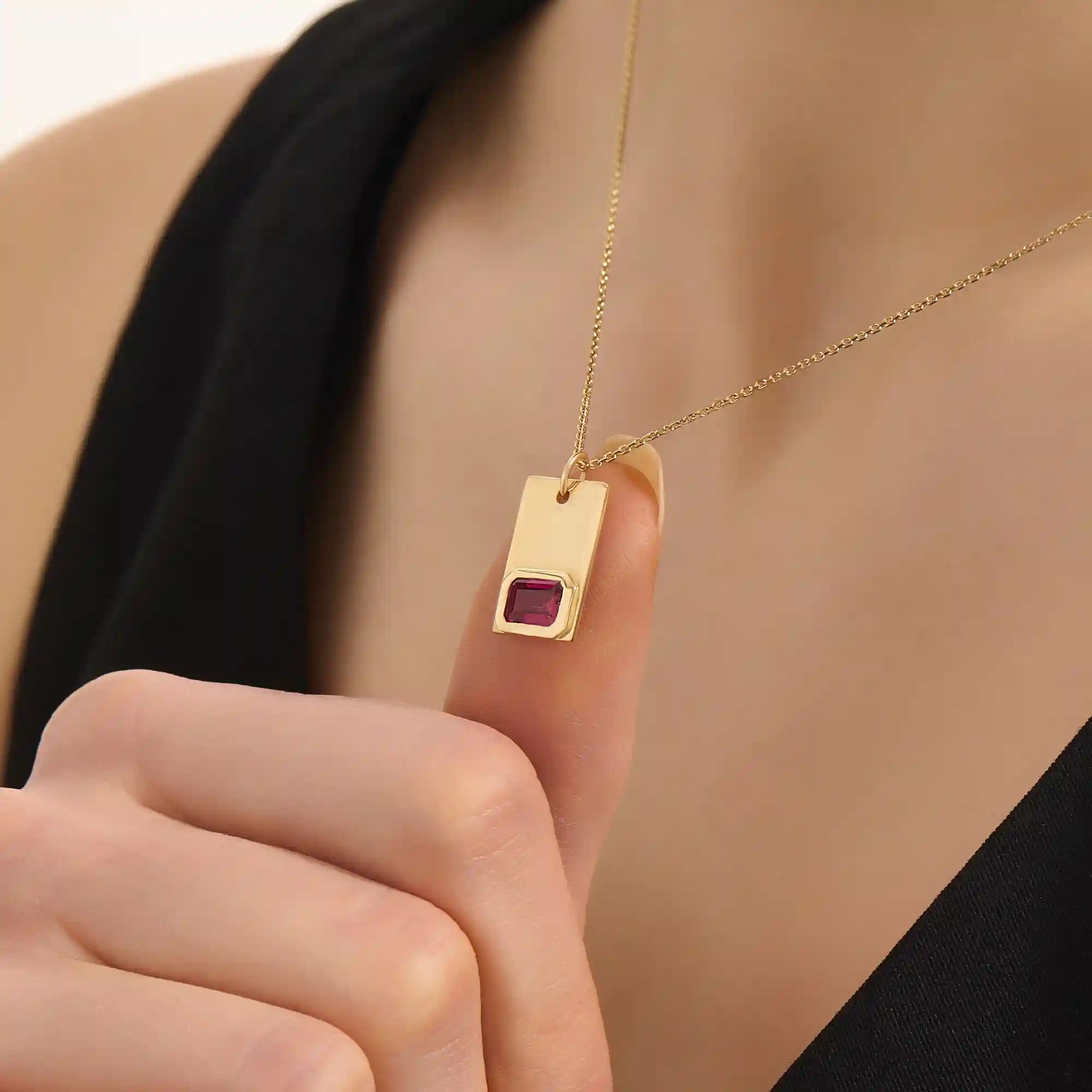 Woman wearing a 14k solid gold rectangle pendant necklace featuring an emerald-cut lab-created ruby in bezel setting. Striking birthstone jewelry with timeless elegance. Ideal for everyday wear or special occasions.
