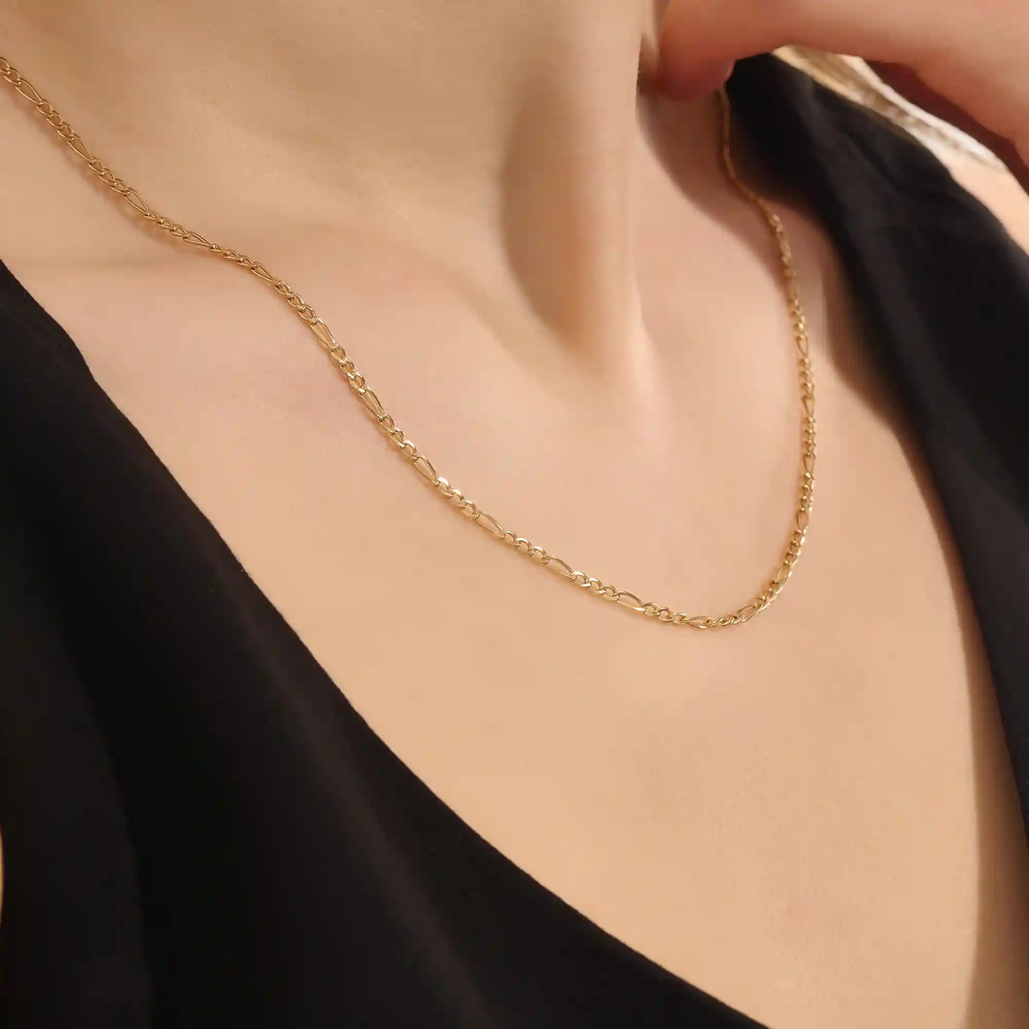 Woman wearing a 14k solid gold slim Figaro chain necklace with a delicate, timeless link pattern. Subtle and elegant for everyday styling. Great on its own or stacked.