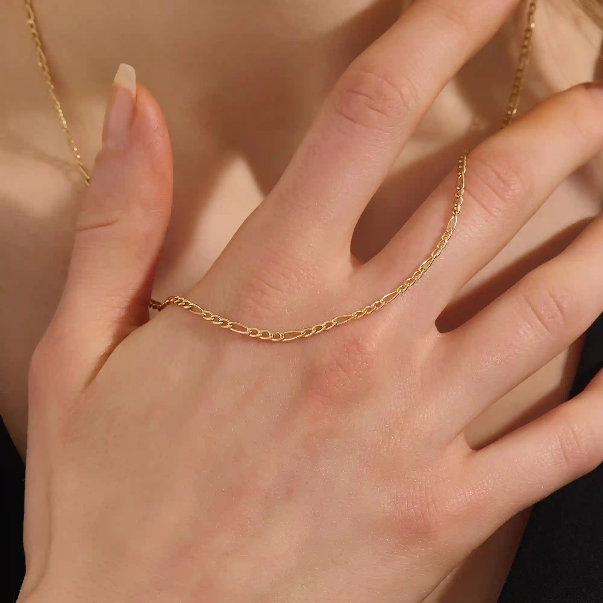Woman wearing a 14k solid gold slim Figaro chain necklace with a delicate, timeless link pattern. Subtle and elegant for everyday styling. Great on its own or stacked.
