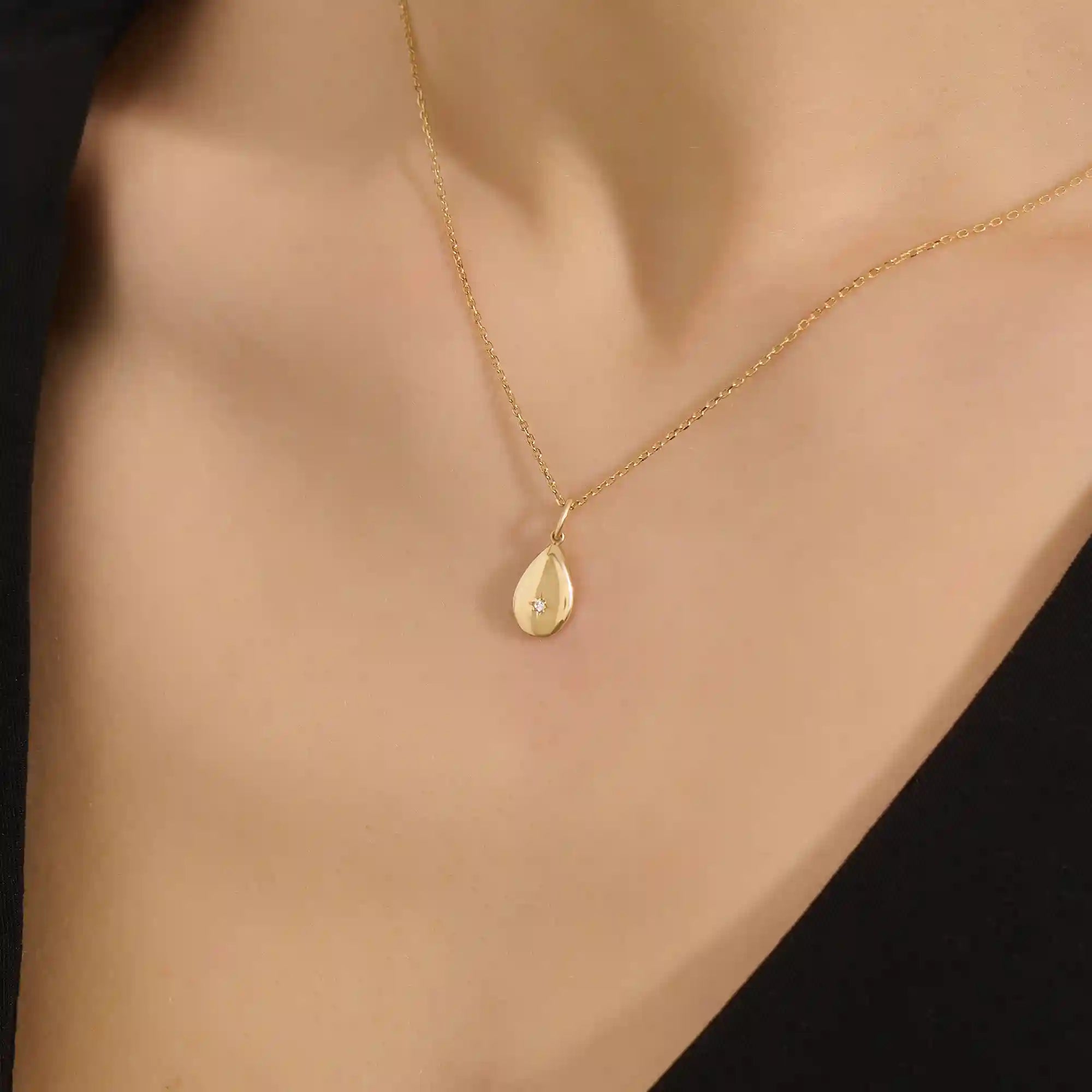Woman wearing a 14k solid gold teardrop necklace with a tiny moissanite centerpiece. Elegant and dainty gold pendant for daily style. Subtle sparkle for modern looks.