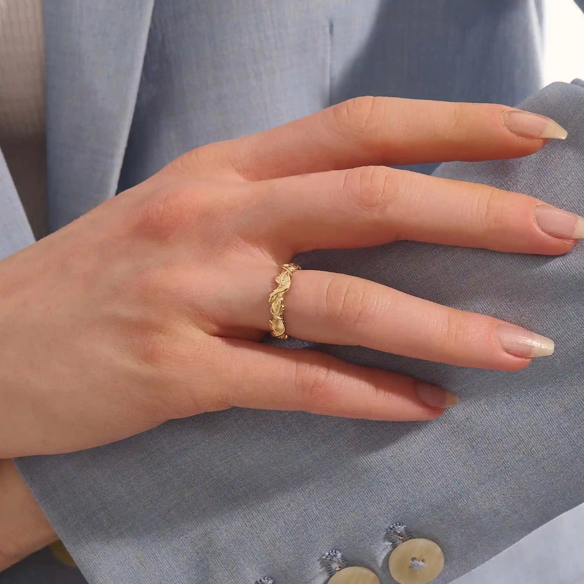 Close-up of a woman's hand wearing a 14k solid yellow gold ivy leaf wedding band. The detailed leaf motifs and smooth polished interior reflect a blend of natural inspiration and artisan craftsmanship, making it a distinctive and elegant choice for daily wear or special occasions.