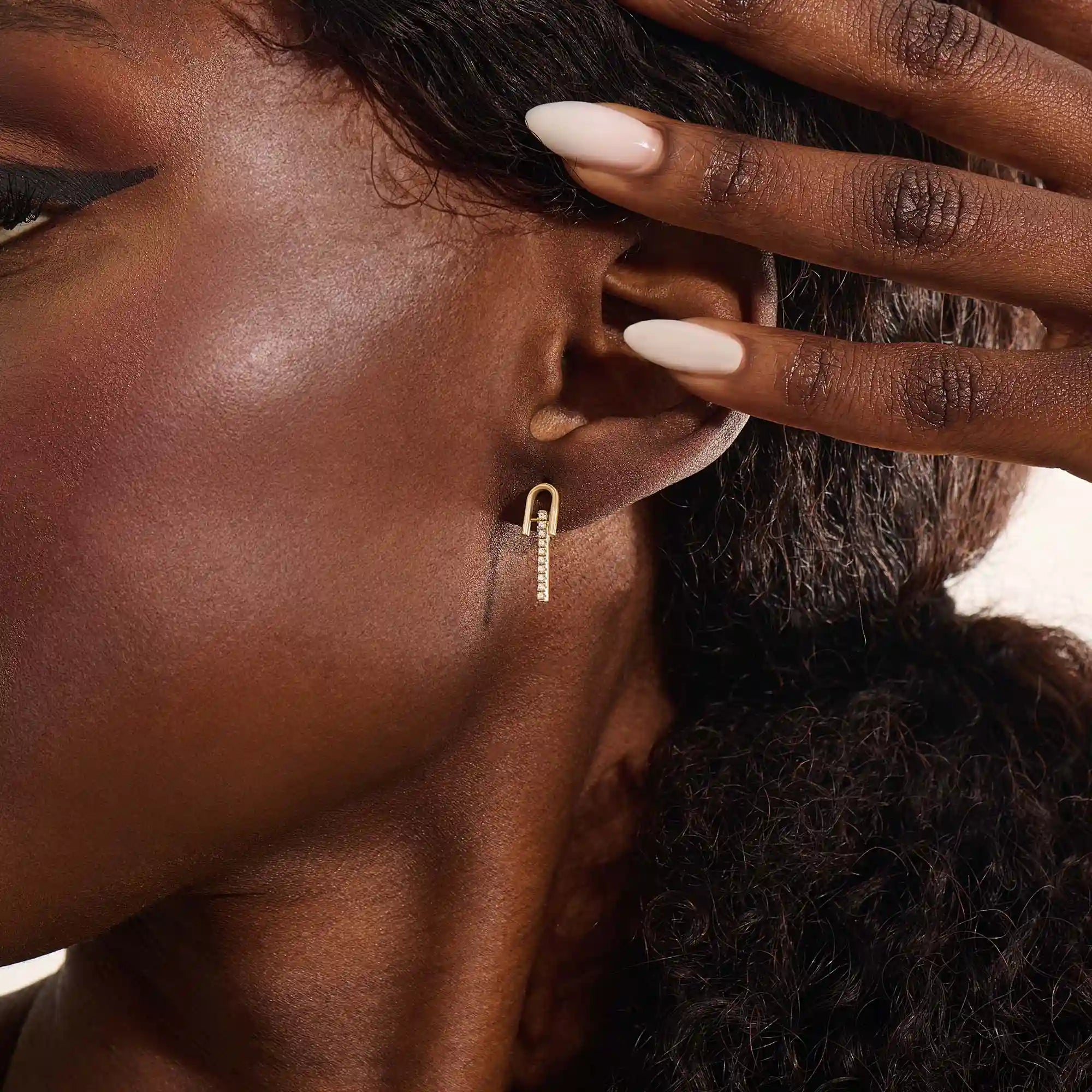 Close-up of a model wearing a 14k yellow gold U-top bar stud earring with a line of brilliant moissanite stones.