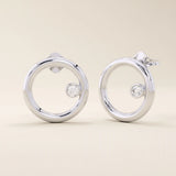 14k solid white gold open circle stud earrings featuring a floating bezel-set round moissanite accent.
