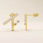 14k solid yellow gold asymmetrical line stud earrings with a horizontal row of round-cut moissanite and a single vertical baguette-cut moissanite accent.
