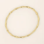 14k solid yellow gold bangle bracelet featuring a twisted, wave-like design that catches the light from every angle, offering a fluid and elegant aesthetic.
