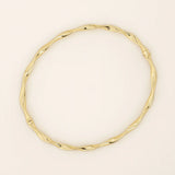14k solid yellow gold bangle bracelet featuring a twisted, wave-like design that catches the light from every angle, offering a fluid and elegant aesthetic.
