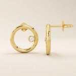 14k solid yellow gold circular karma stud earrings with a single bezel-set round moissanite floating at the inner edge of each hoop.
