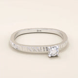 14k white gold promise ring with a round moissanite center stone in a four-prong setting, textured band design, modern solid gold jewelry.

