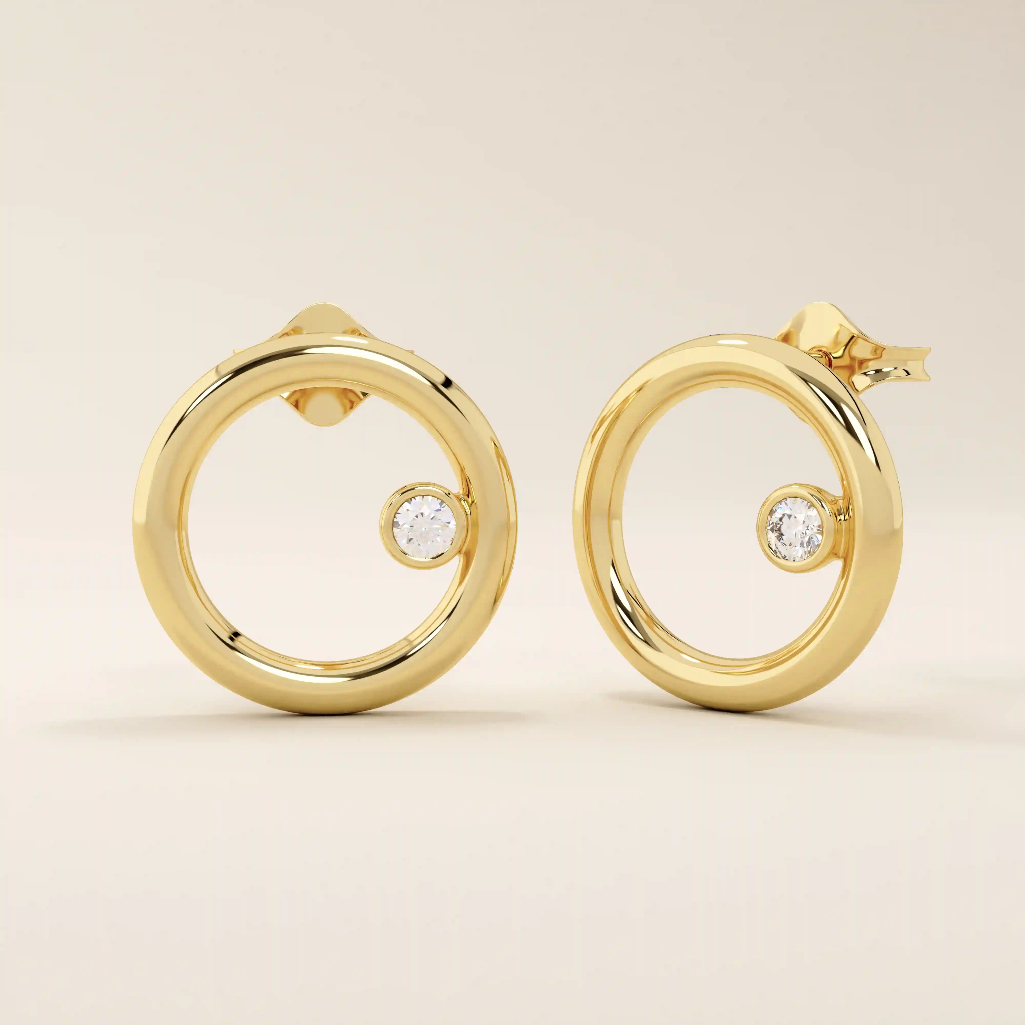 Angled view of 14k yellow gold polished circle stud earrings with an off-center bezel-set moissanite accent.
