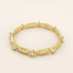 Angled view of a 14k yellow gold band showcasing alternating moissanite stones and polished leaf designs.
