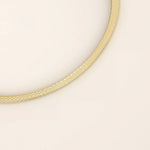 Angled view of a 14k yellow gold textured square tube bangle highlighting its slim tubular form and shimmering surface detail.
