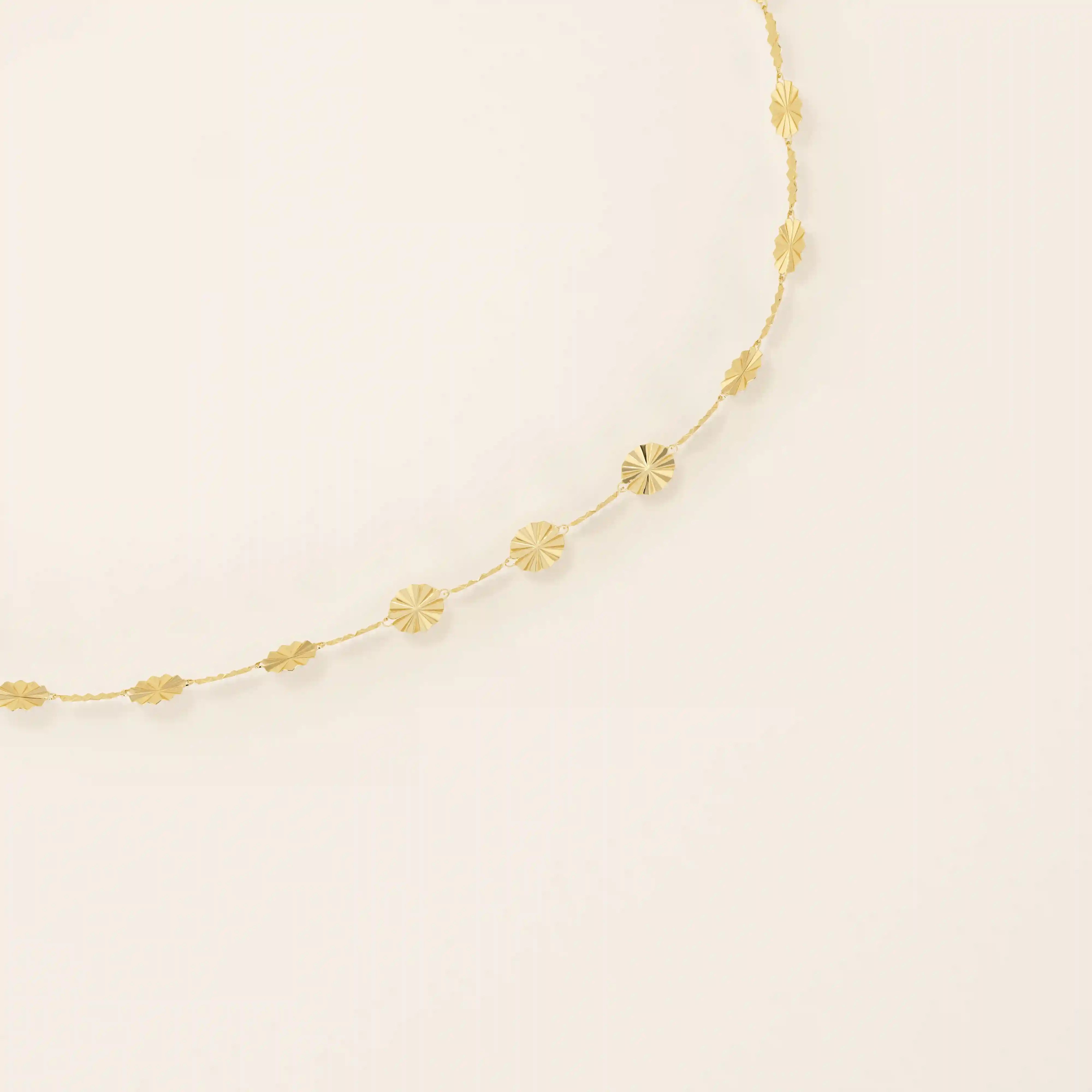 Close-up of a 14k gold textured chain bracelet highlighting the intricate starburst engraved discs.
