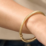 Close-up of a model’s arm wearing a 14k yellow gold rope bangle bracelet with a twisted rope design and polished shine.
