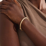 Close-up of a model’s arm wearing a 14k yellow gold rope bangle bracelet with a twisted rope design and polished shine.
