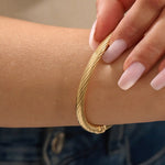 Close-up of a model’s arm wearing a 14k yellow gold rope bangle bracelet with a twisted rope design and polished shine.
