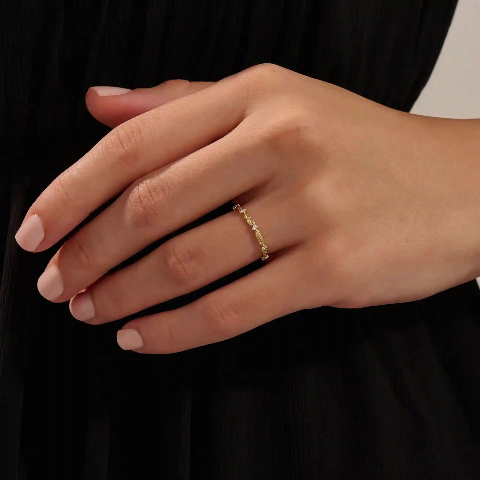 Close-up of a model’s hand wearing a 14k yellow gold ring with moissanite stones and engraved leaf motifs.
