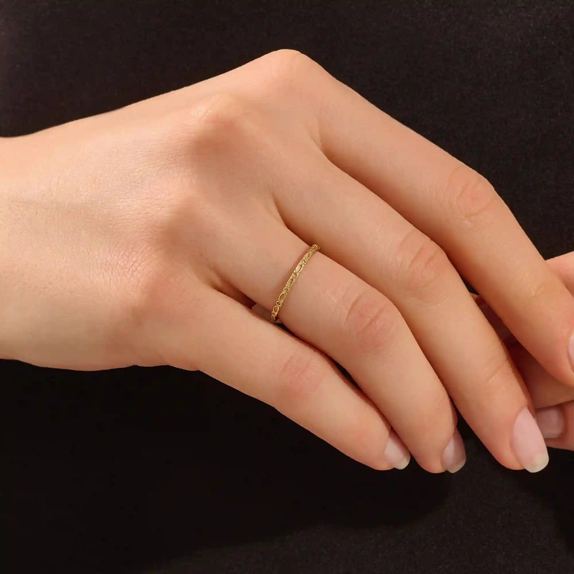 Close-up of a model’s hand wearing a 14k yellow gold slim wedding ring with a marquise-style engraved design.
