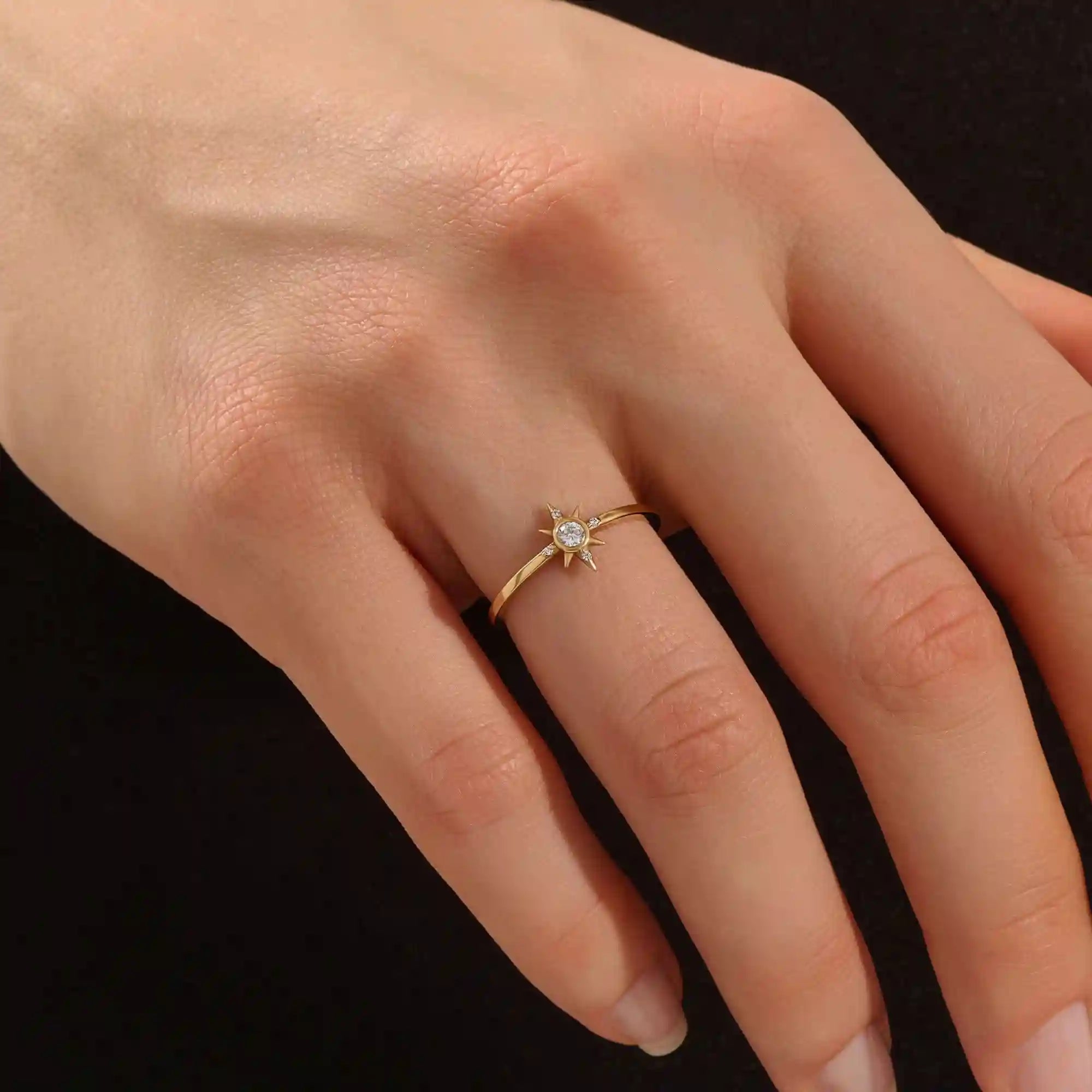 Close-up of a model’s hand wearing a 14k yellow gold starburst ring with moissanite center and accent stones.
