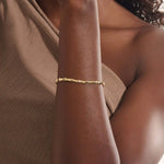 Close-up of a model’s wrist wearing a 14k yellow gold bone bracelet with bold curved links in a polished statement design.

