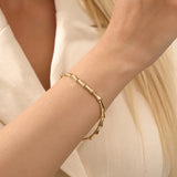 Close-up of a model’s wrist wearing a 14k yellow gold bone bracelet with bold curved links in a polished statement design.
