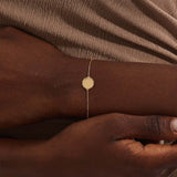 Close-up of a model’s wrist wearing a 14k yellow gold sun bracelet with a round medallion and delicate chain design.
