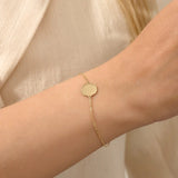 Close-up of a model’s wrist wearing a 14k yellow gold sun bracelet with a round medallion and delicate chain design.
