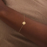 Close-up of a model’s wrist wearing a 14k yellow gold sun bracelet with a round medallion and delicate chain design.

