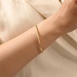 Close-up of a model’s wrist wearing a 14k yellow gold textured square tube bangle with a slim geometric band and polished finish.
