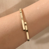 Close-up of a model’s wrist wearing a 14k yellow gold wrap-around bangle with a polished finish and overlapping band detail.
